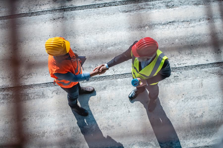 a manager and foreman on a concrete construction site shaking hands