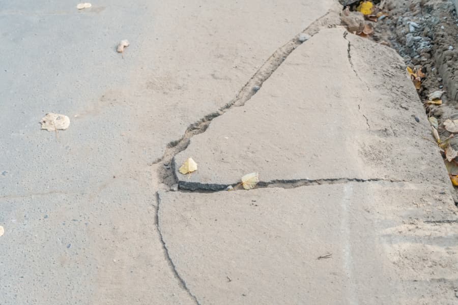 large crack on a concrete sidewalk sprinkled with leaves