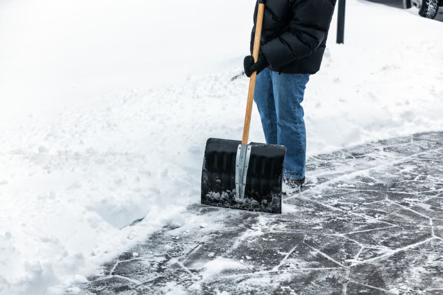 a person in winter clothing shoveling snow from a concrete sidewalk