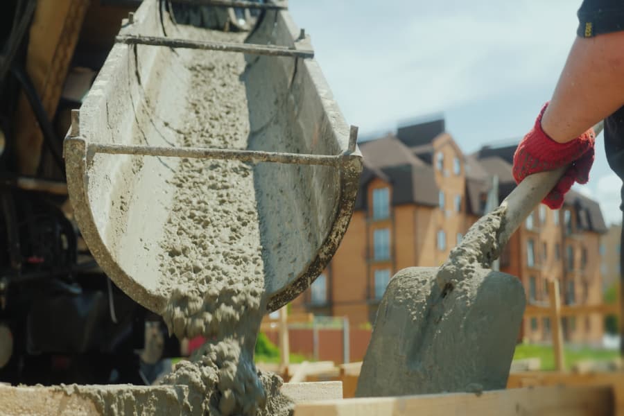 Workers taking ready-mix concrete from a mixer into a wooden formwork.